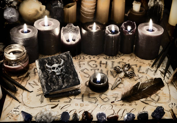 istock Evil book with black magic spells, candles and ouija board on witch table. 1221553598