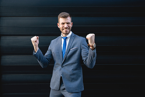 Portrait of excited young businessman looking forward with raised hands.