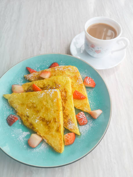 Triangular French toast with strawberry and syrup on a blue plate with coffee, homemade breakfast