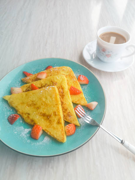 Triangular French toast with strawberry and syrup on a blue plate with coffee, homemade breakfast