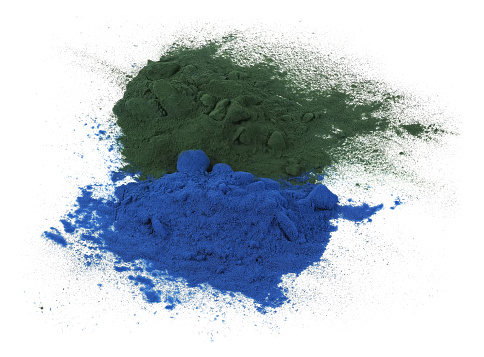 Heaps of green and blue spirulina powder, isolated on white background