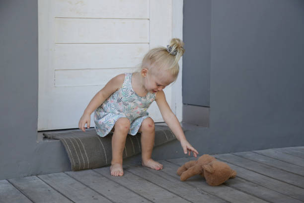 una niña sentada afuera sola tratando de buscar a su osito de peluche. concepto de niño abusado. - child physical injury teddy bear wound fotografías e imágenes de stock