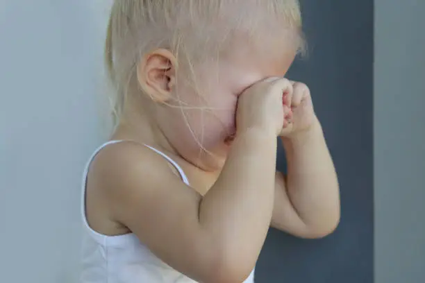 Photo of Close up candid portrait of upset crying toddler girl covering eyes with hands