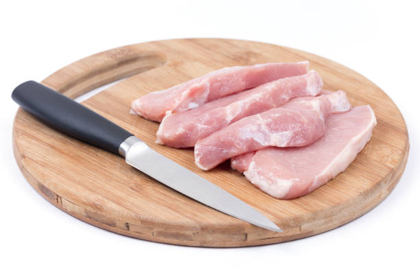Three raw pork chops with kitchen knife on the wooden cutting board.