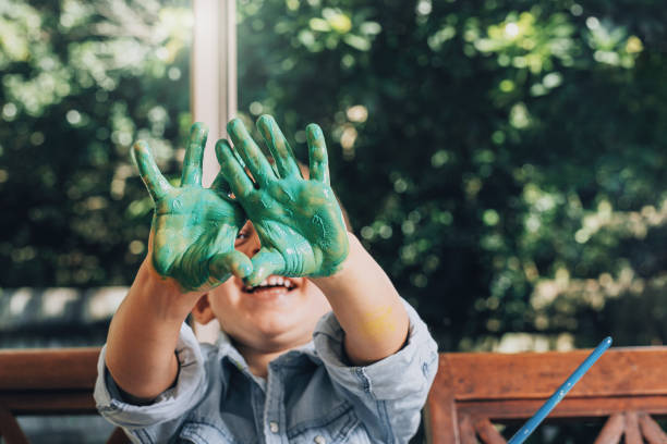 menino com as mãos pintadas em tintas verdes prontas para fazer impressões manuais - preschool child craft preschooler - fotografias e filmes do acervo