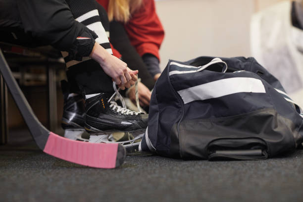 Hockey Player Getting Ready Close up of unrecognizable young woman tying shoelaces on skates while preparing for hockey practice in locker room, copy space skater feet stock pictures, royalty-free photos & images