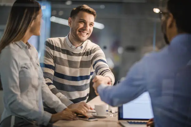 Happy couple having a meeting with their real estate agent while men are shaking hands. The view is through glass.