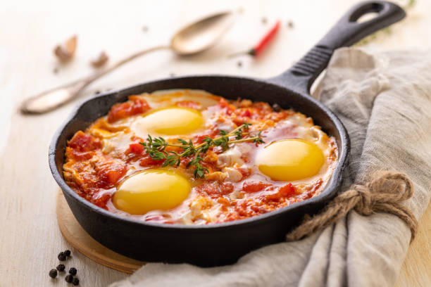 Shakshuka. Fried eggs with tomatoes and sweet pepper and herbs in a serving cast-iron frying pan. stock photo