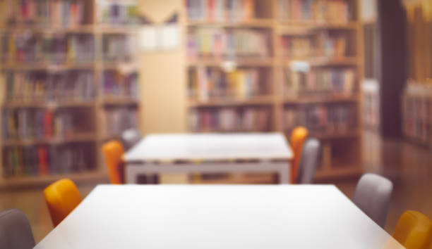 istock Empty White wooden table  ready for your product display montage. with book shelf in library blurred background. Blurry perspective view of educational study room space with book shelves. 1221579297