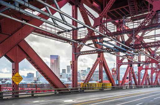 Drawbridge transportation and pedestrian Broadway bridge over the Willamette River in Portland with interlocking metal trusses and tram rails and a view of the city down town with a cloudy sky