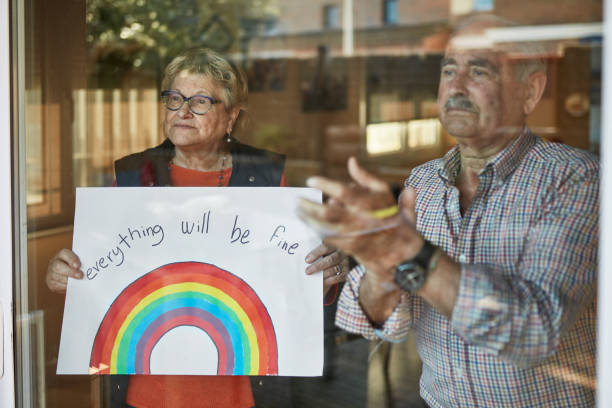 istock Senior couple applauding and showing a hand drawn rainbow at home in quarantine 1221581294