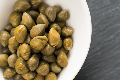 the famous and small capers of pantelleria prepared in a white bowl on a black slate top