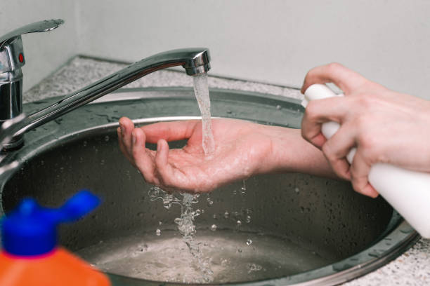istock Woman squeezes soap from a white bottle onto her hand. Man using alcohol gel as a hand sanitizer. A stream of clean water drains into the sink. Hand washing with soap to prevent coronavirus. 1221585551