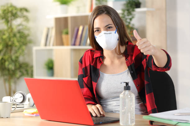 istock Student with mask due covid-19 gesturing thumbs up at home 1221585600