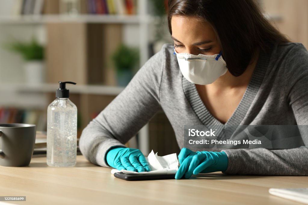 Woman disinfecting phone from coronavirus at night at home Woman with gloves and protective mask disinfecting smart phone from coronavirus sitting on a desk at night at home Obsessive-Compulsive Disorder Stock Photo