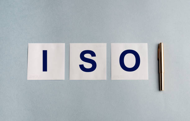 istock ISO letters on white stickers and pen on blue grey background 1221586900