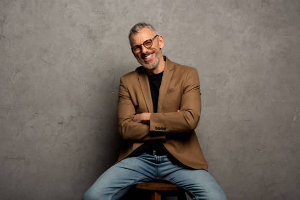 bearded businessman in glasses looking at camera and sitting with crossed arms on grey bearded businessman in glasses looking at camera and sitting with crossed arms on grey blazer jacket stock pictures, royalty-free photos & images