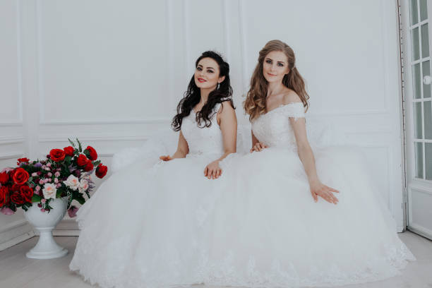 istock two brides in wedding dresses sit on a white couch 1221593500
