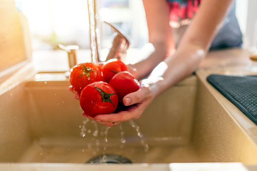 Young woman washes vegetables in domestic kitchen. Woman prepared a dinner in the kitchen. Healthy eating concept. Woman washing fresh vegetables tomatoes, preparation salad vegetarian meal