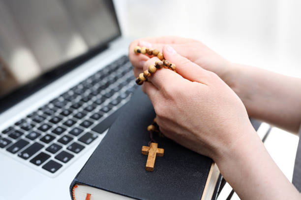 Rosary prayer online, holy mass conducted online. A woman prays on a rosary in front of a computer. rosary beads stock pictures, royalty-free photos & images