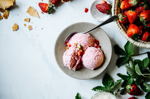 Directly above shot of freshly made strawberry ice-cream on table with ingredients around. Tasty strawberry ice-cream in a bowl on table.