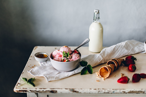 Strawberry ice cream in a bowl with waffle cone, milk bottle and strawberries on table. Freshly made strawberry icecream on table with ingredients around.