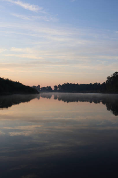 Beautiful calm sunrise dawn by the river with reflection on mirror water. Nice pastel colors nature landscape. Trees silhouette, fog, clouds and sunset photo.