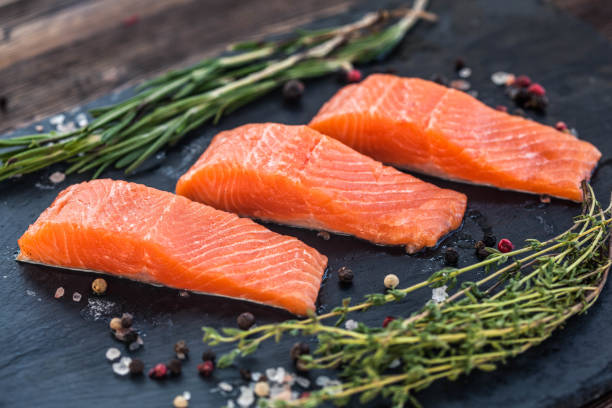 istock Three salmon steakes with thyme, rosemary, pepper and salt grains on the black board 1221610002