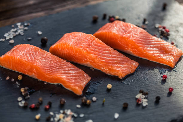 istock Three salmon steakes with thyme, rosemary, pepper and salt grains on the black board 1221610167