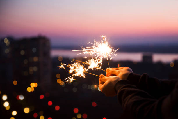 istock Hands with sparkles Bengal fire  that bokeh cities background. standing in home. chelter in place. end of a quarantine. home holiday 1221611548