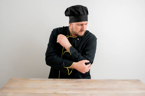 istock Young male chef in black uniform has elbow pain 1221614961