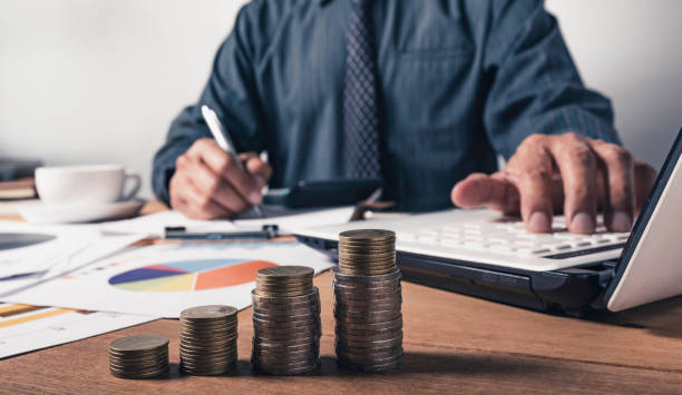 istock Business man working and writing on notebook with stack of coins for financial and accounting concept. 1221617321