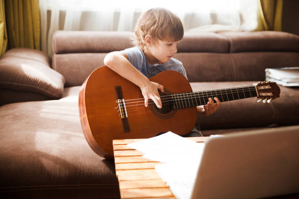 istock Kid  boy playing  guitar and watching  online lessons  on laptop while practicing at home.  Stay home. quarantine. Online training, online classes. 1221617637