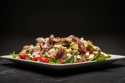 Photography of a healthy steak salad with black background.