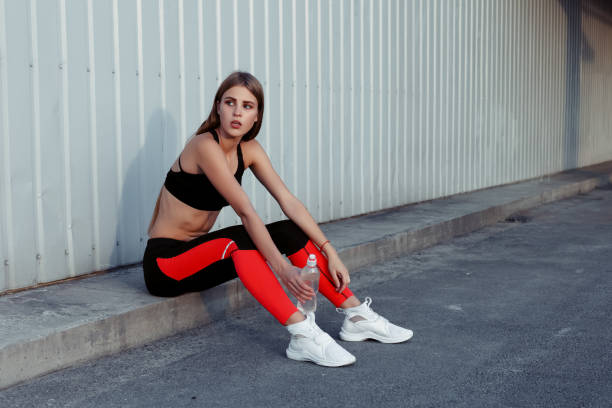 istock Female athlete drinking water while standing by a grey wall. 1221617918
