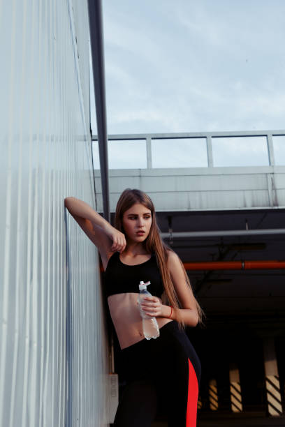 istock Female athlete drinking water while standing by a grey wall. 1221618129