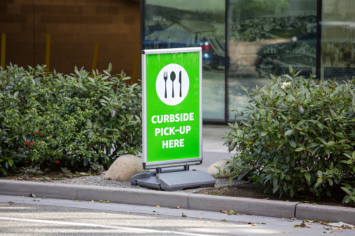 The city of Seattle is one of the epicenters of the coronavirus COVID-19 outbreak.  The government shutdown of non-essential businesses has closed many public places but restaurants that provide takeout meals as an essential service can remain open.  This curbside pickup sign outside of Amazon headquarters indicates the location for patrons to stop for their food.