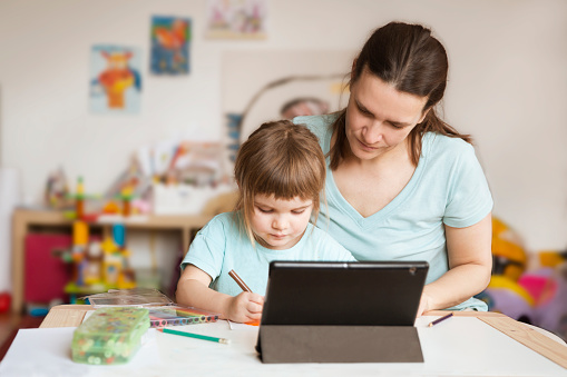 Little girl draws paints  with her mother And watches a drawing lesson online on a tablet at home. The concept of distance learning online school.