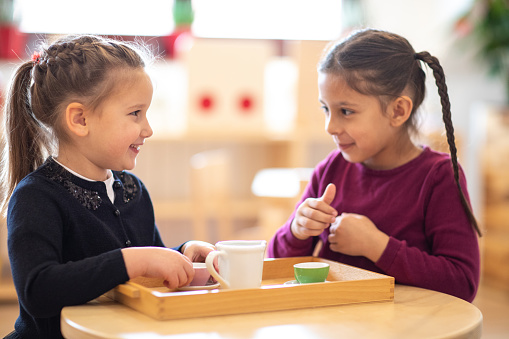 Two cute girls pretending to have tea party in day care playroom