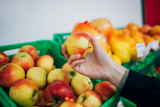 istock Female hand holding ripe apple next to fruit shelves 1221625687