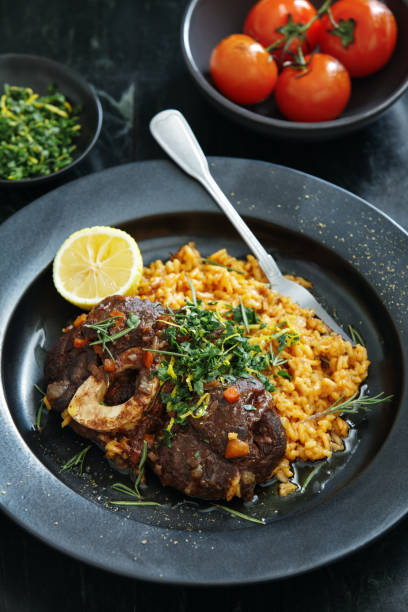 Traditional Italian Osso Buco with Creamy Saffron Risotto and Gremolata Traditional Italian Osso Buco with Creamy Saffron Risotto dish topped with fresh parsley, garlic and lemon zest. Close-up composition on dark background ossobuco stock pictures, royalty-free photos & images