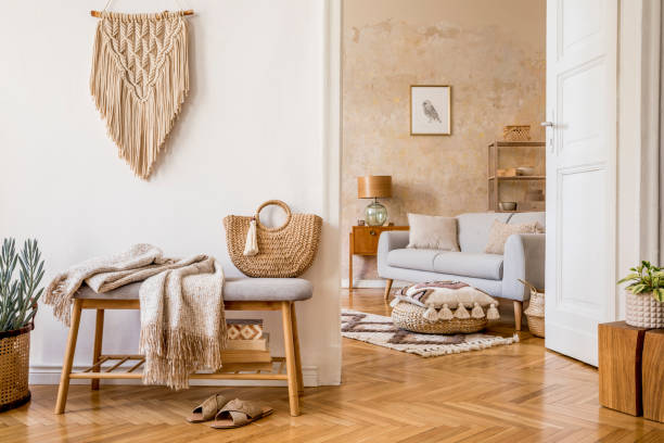 Scandinavian interior of open space with wooden bench, grey sofa, pillows, palid, picture frame, macrame, plant, books, carpet, decoration and elegant personal accessoreis in stylish home decor. Interior design of boho living room. Oriental concept of home decor. Wabi sabi. boho stock pictures, royalty-free photos & images