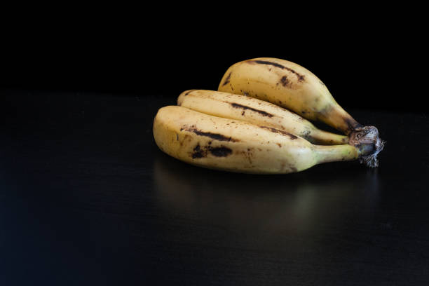 três bananas na mesa preta com luz escura. comida de vida morta. pictórica. comida escura - autumn banana breakfast close up - fotografias e filmes do acervo
