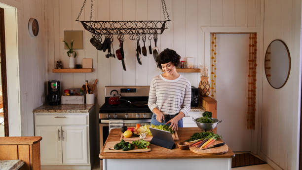 Smiling young woman using fresh vegetables while preparing a healthy meal Smiling woman standing at an island in her kitchen at home chopping an assortment of fresh vegetables for a healthy meal chopping food photos stock pictures, royalty-free photos & images