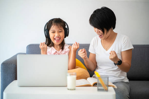 Asian girl and her teacher using laptop for online study during homeschooling at home stock photo
