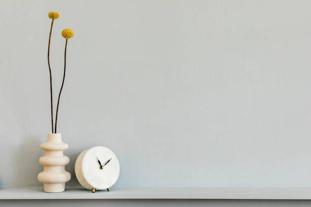 istock Minimalistic composition on the shelf with dried flower in design vase and white clock. Grey wall. Copy space. 1221630966