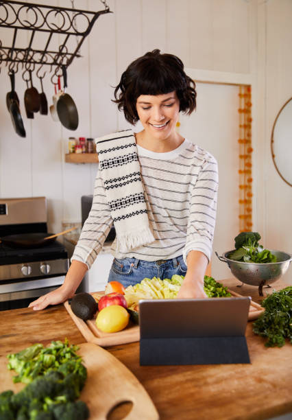 istock Smiling young woman reading an online recipe while making dinner 1221632533