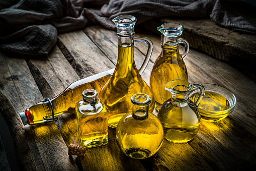 Collection of extra virgin olive oil bottles shot on rustic wooden table. Predominant colors are gold and brown. High resolution 42Mp studio digital capture taken with SONY A7rII and Zeiss Batis 40mm F2.0 CF lens