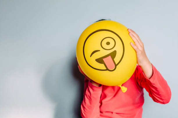Child holding yellow balloon in the hands Unrecognizable person holding yellow balloon against blue background sticking out tongue photos stock pictures, royalty-free photos & images