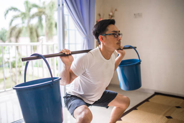 an asia chinese man doing squat workout by using bucket instead of gym weights equipment training at home due to coronavirus covid-19 pandemic lockdown issue. - 2127 imagens e fotografias de stock